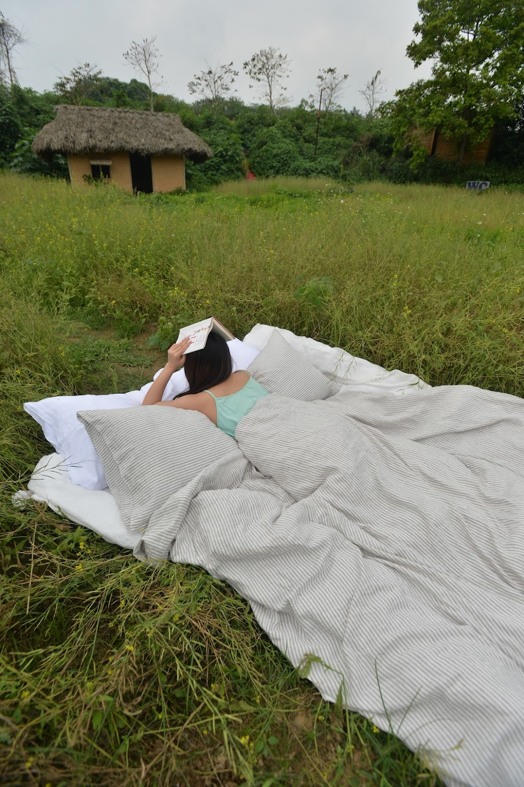 Woman reading outdoors on SCANDALINEN linen bedding in a natural meadow setting