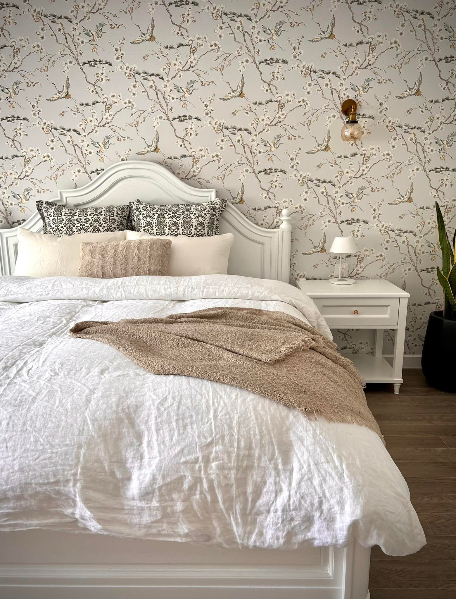 French country bedroom with white linen duvet, floral bird wallpaper, and white timber bed frame