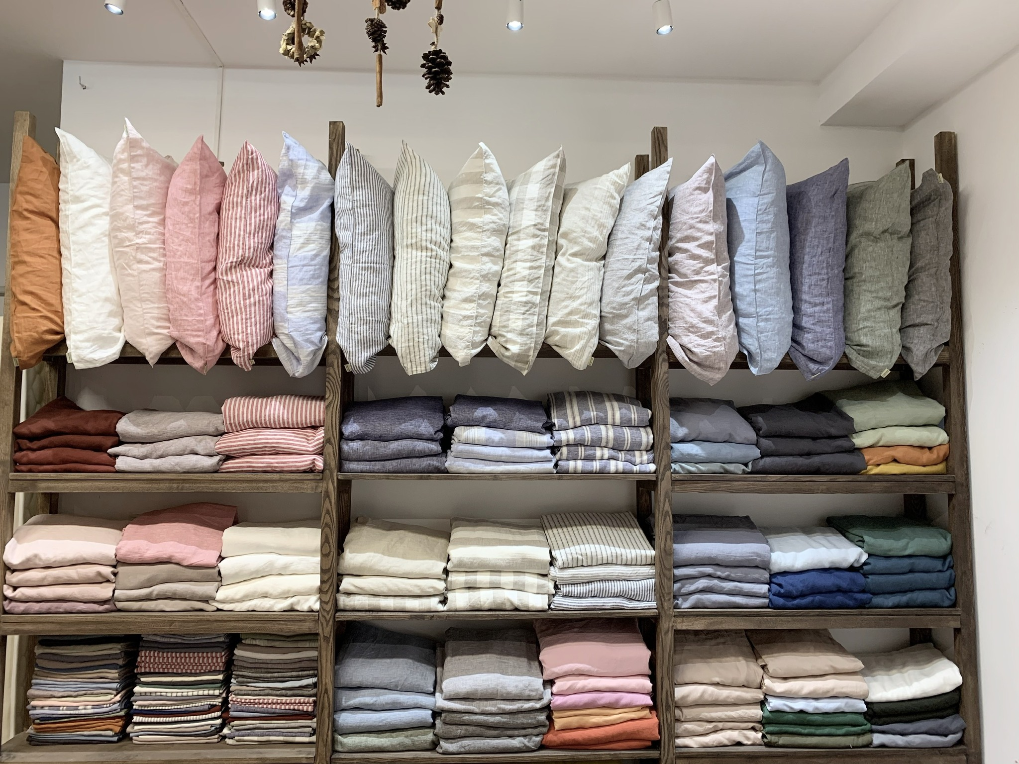 SCANDALINEN linen showroom wall with 50 colors of French linen pillowcases and folded duvet covers on wooden shelves