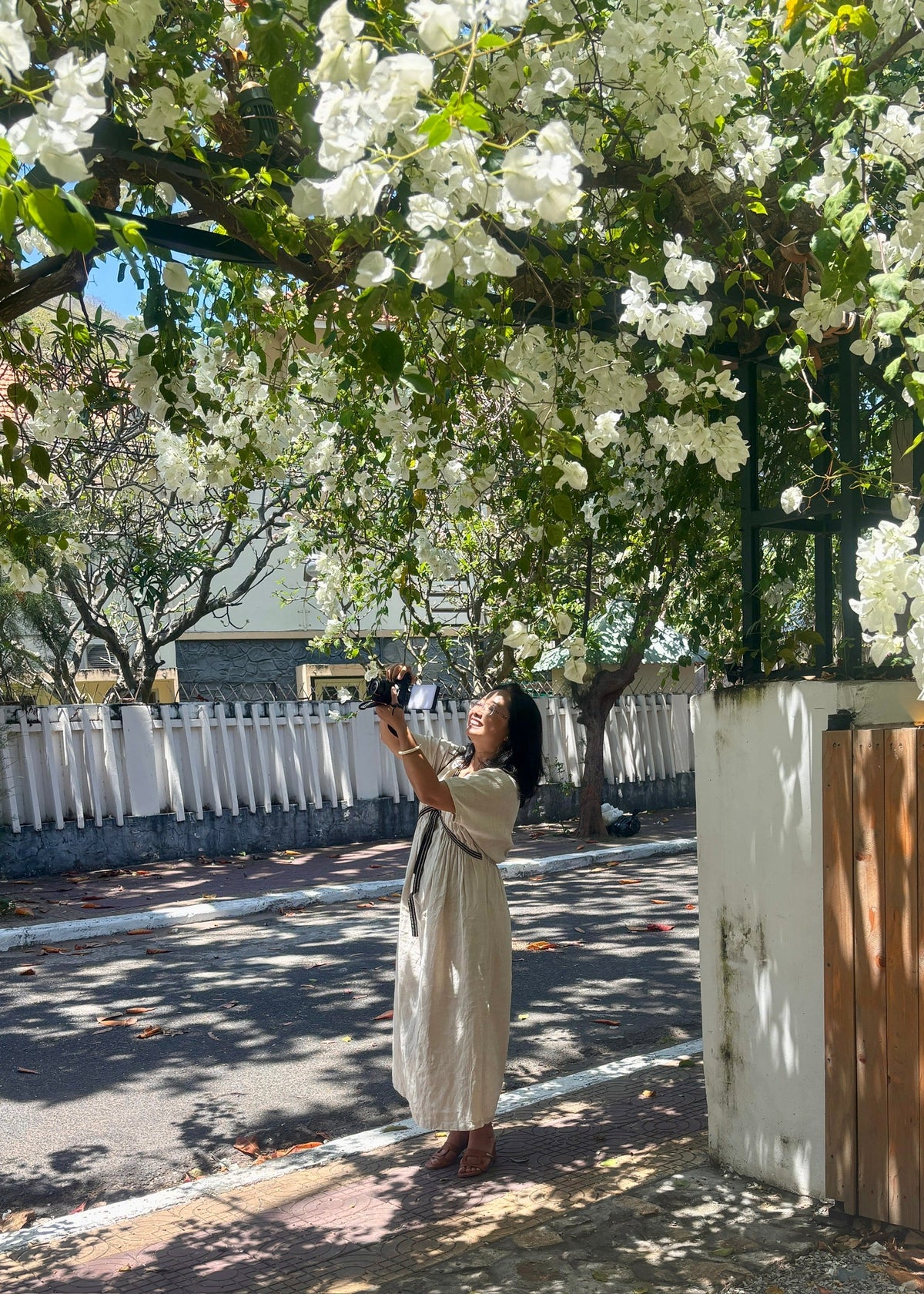 Woman in a natural linen dress photographing white bougainvillea in strong tropical sun