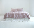 Dusty pink French linen duvet cover and matching pillows on a bed with a white bed skirt, shown in natural daylight.