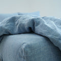 Blue linen bedding at the edge of a mattress, with a folded duvet above the sheet.