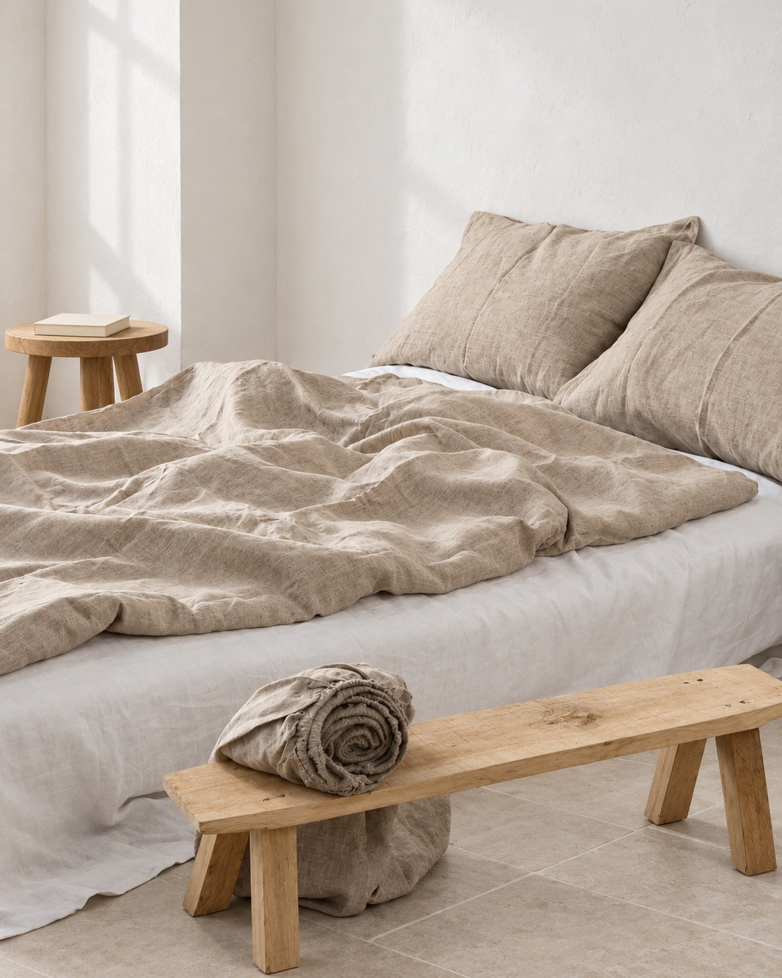 Natural flax French linen duvet cover and matching pillows with visible woven texture, styled beside an oak bench in a white studio